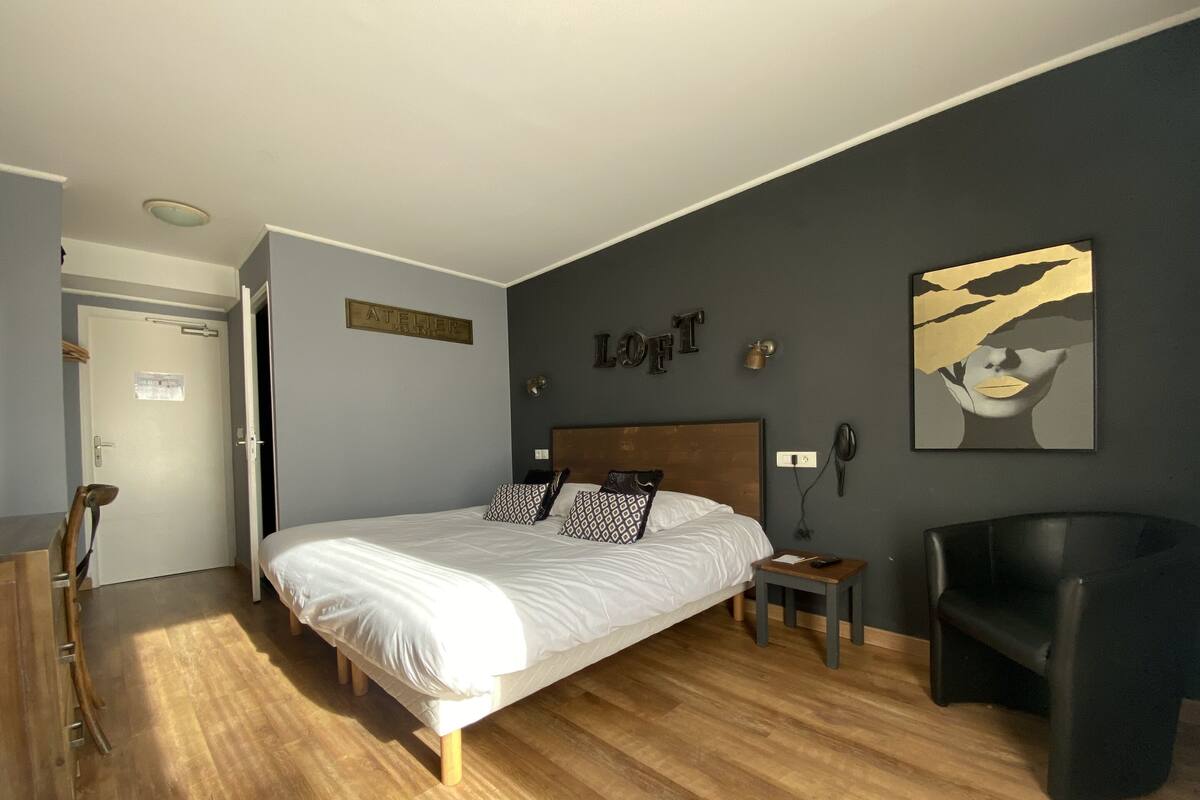 A bedroom with a bed, a bedside table, a chair, a desk, and a door.