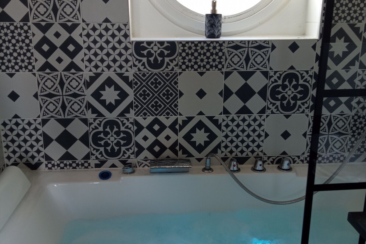 A bathroom with a bathtub, a window, and patterned tiles.