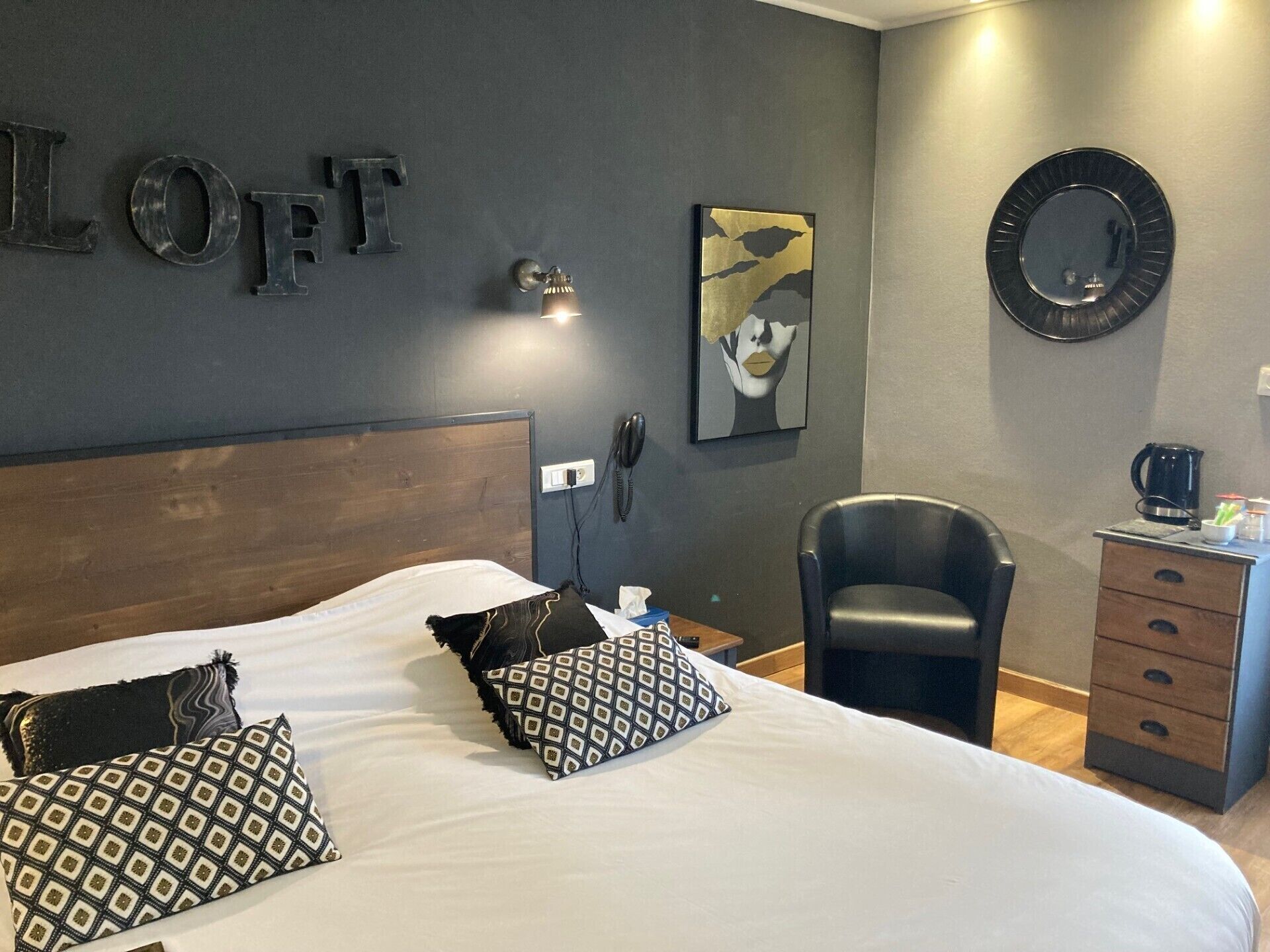 A hotel room with a large bed, a desk with a coffee maker, a chair, and a wall-mounted phone.