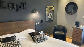 A hotel room with a large bed, a desk with a coffee maker, a chair, and a wall-mounted phone.