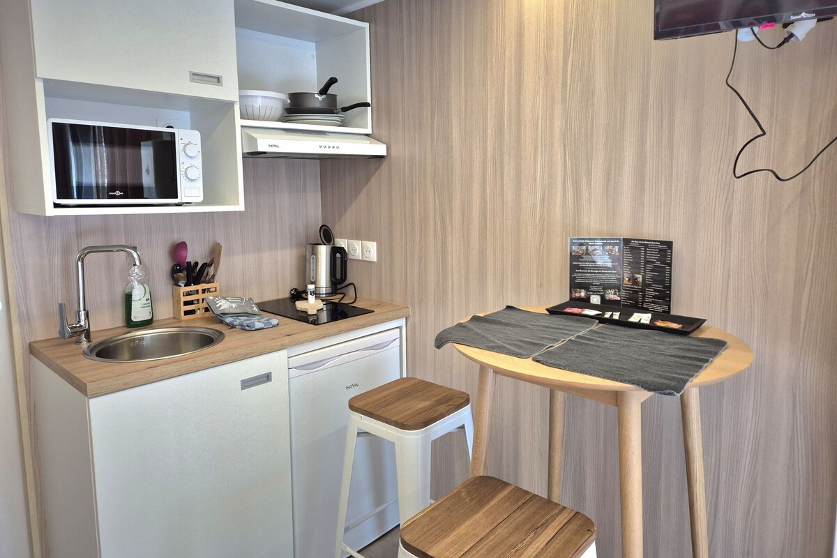 Une petite cuisine équipée d’un four à micro-ondes, d’un évier et d’un petit réfrigérateur. On y trouve également une machine à café sur le plan de travail, ainsi qu’une table avec un menu ou une brochure d’information.
