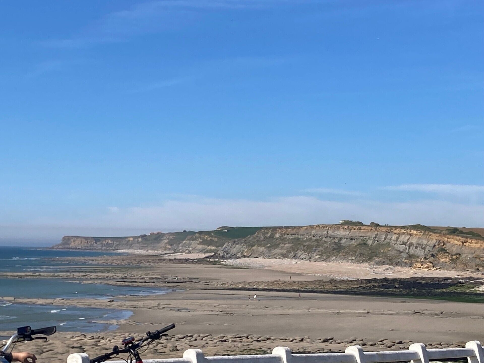 Un paysage côtier avec une plage rocheuse, des falaises et un ciel dégagé.