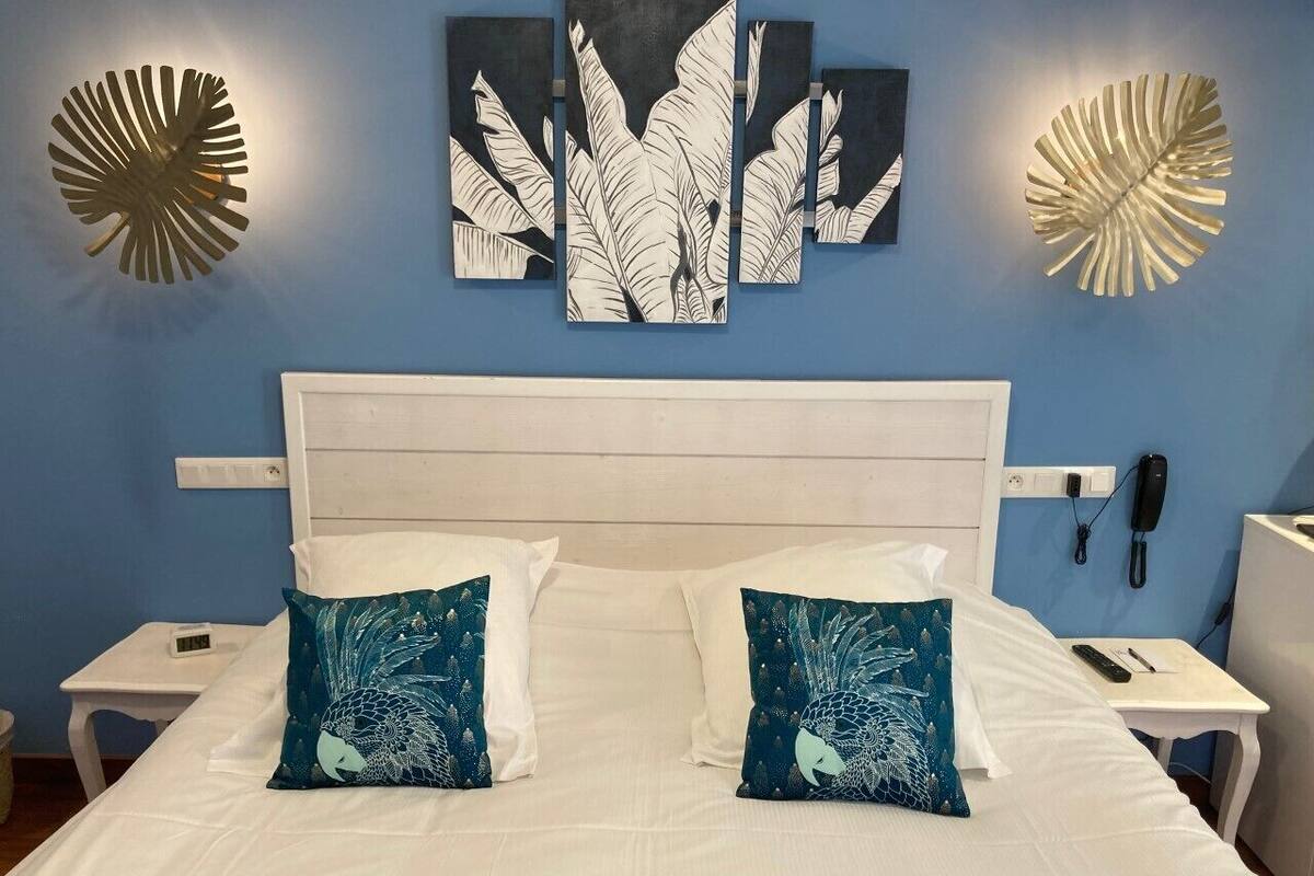 A hotel room with a white bed, two blue patterned pillows, a white headboard, and wall art above the bed.