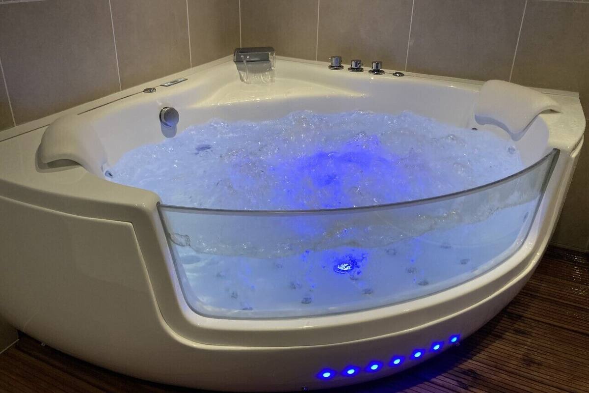 A modern bathtub with a glass panel, blue LED lights, and a water jet system.