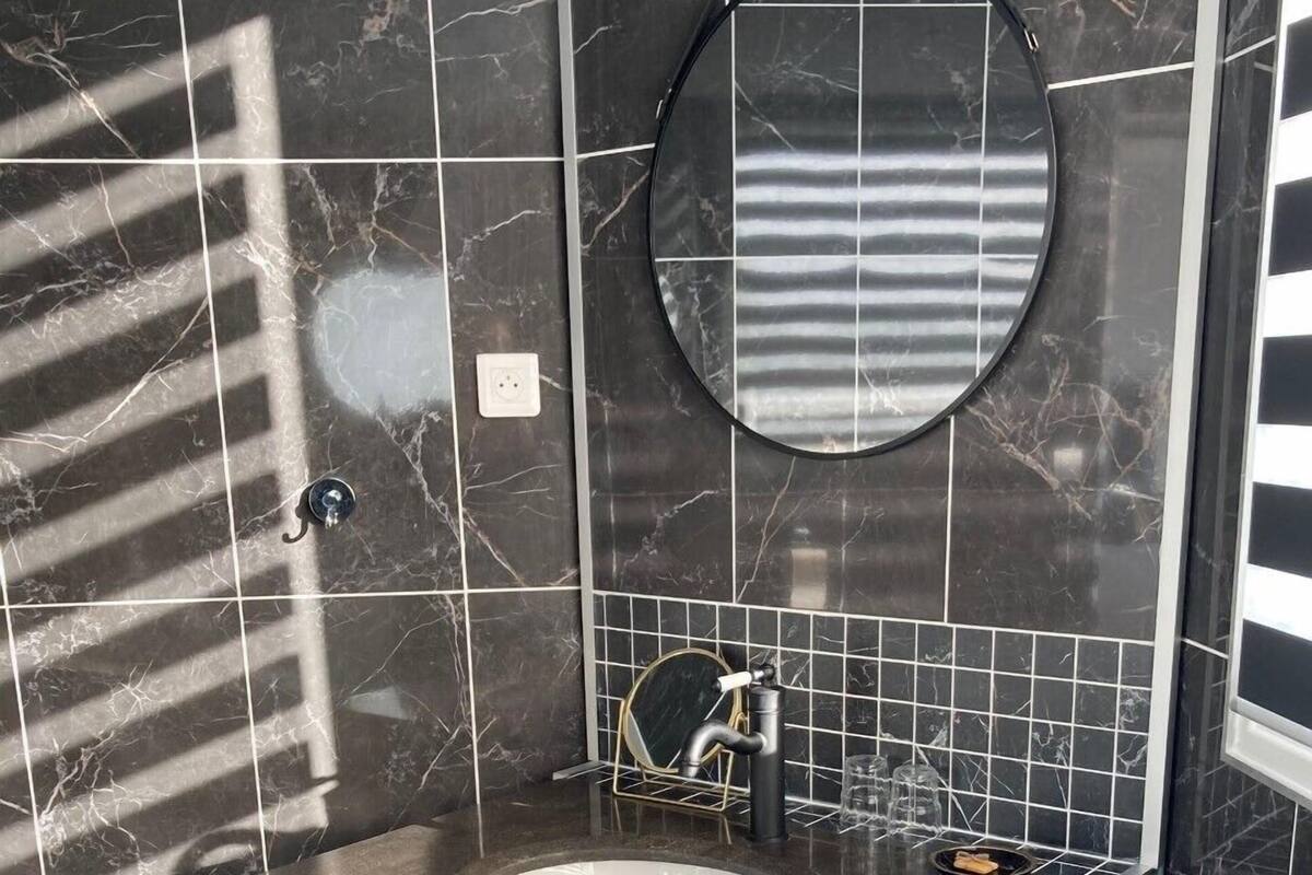 A bathroom with a marble-tiled wall, a round mirror, a sink with a towel, and wooden cabinetry.