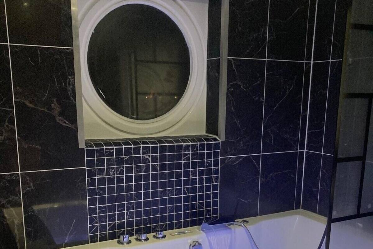 A modern bathroom with a large bathtub, a built-in circular mirror, and a tiled wall.