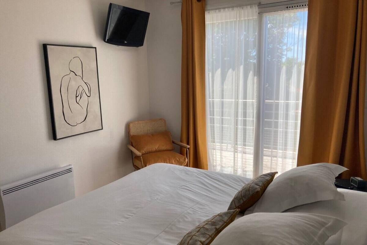 A hotel room with a large bed, a chair, a television mounted on the wall, and a window with curtains.