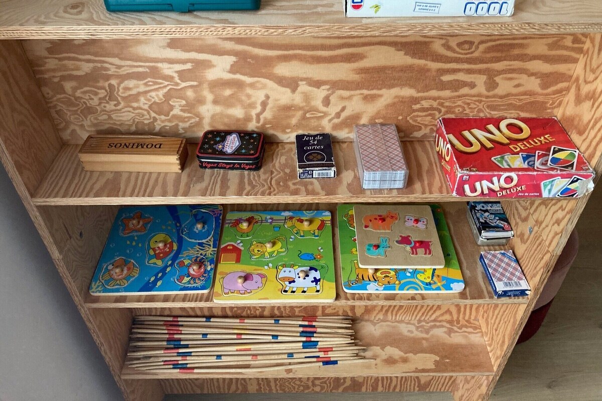 Ein Holzregal mit verschiedenen Gesellschaftsspielen und einer UNO Deluxe Kartenbox.