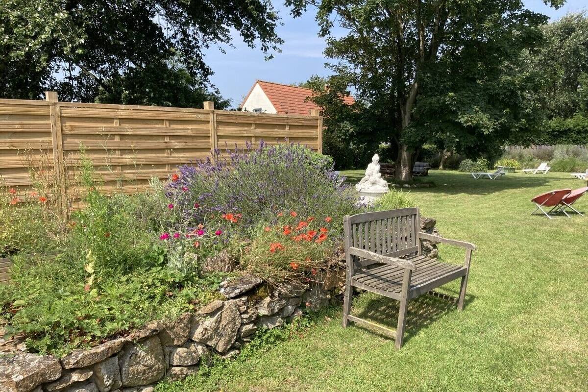 Un giardino con un muro di pietra, una panchina in legno e una statua.