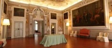 A spacious room with a high ceiling, ornate ceiling details, a large painting, and a green table with chairs.