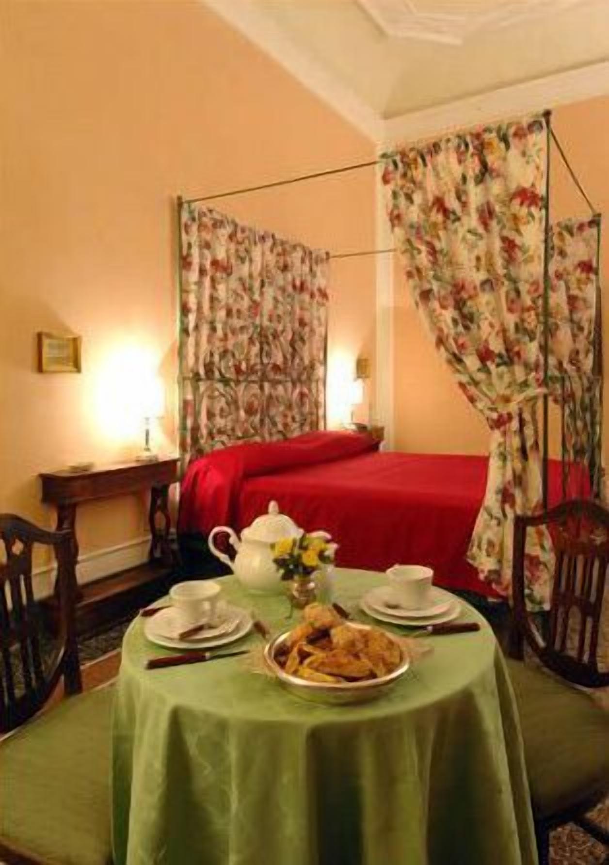 A hotel room with a bed, a table set for breakfast, and floral curtains.