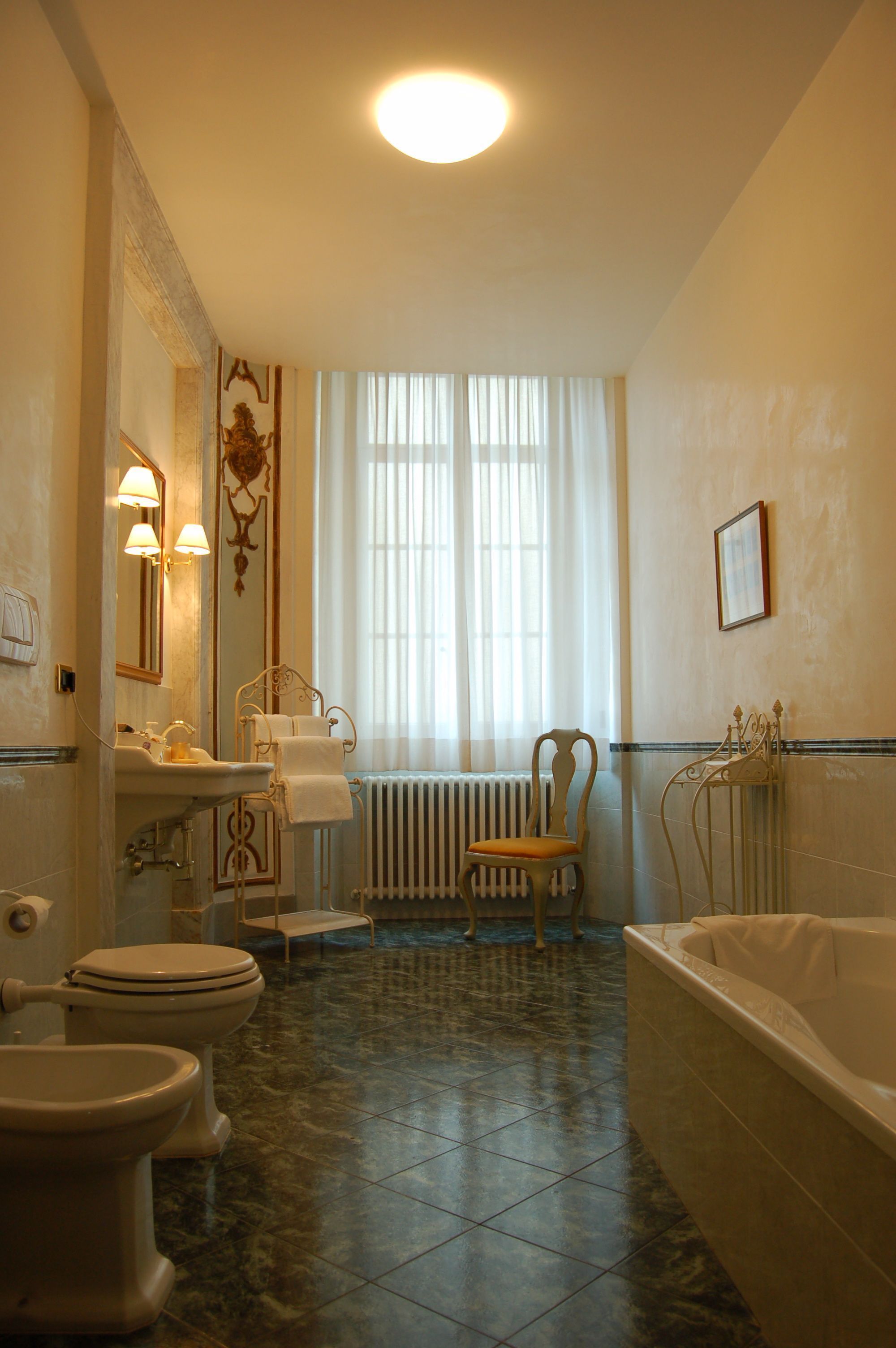 Une salle de bain avec une baignoire, deux toilettes, un lavabo et une chaise.