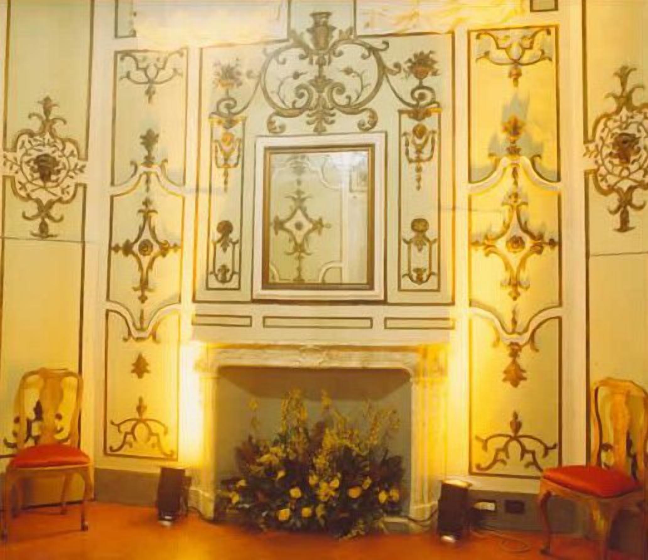 A room with a fireplace, ornate wall decorations, and two chairs with red cushions.