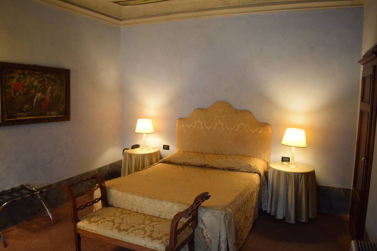 Un dormitorio con una cama, dos mesitas de noche con lámparas, una silla y un cuadro en la pared.