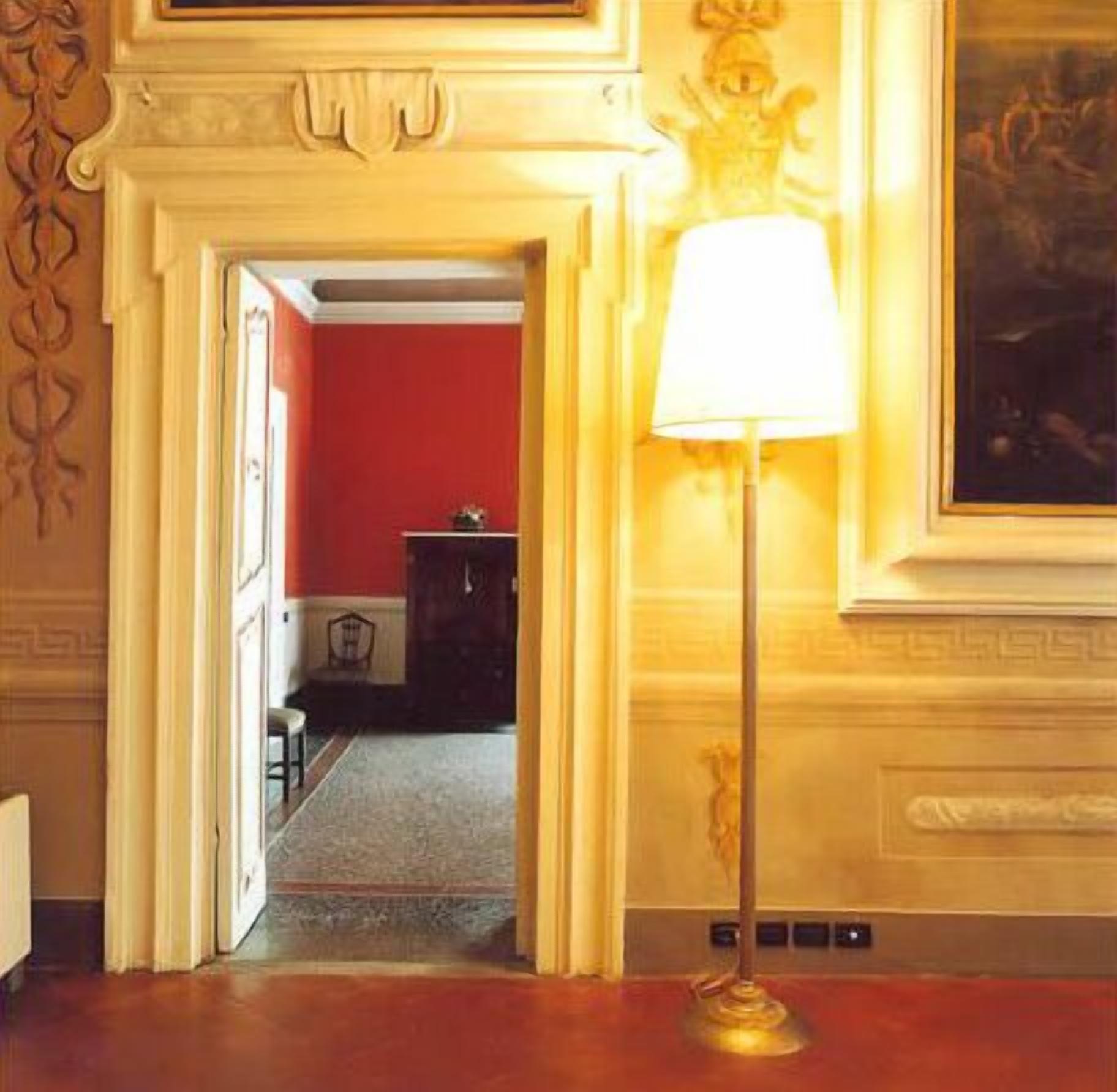 Una habitación con una pared roja, una puerta blanca y una lámpara con pantalla blanca.