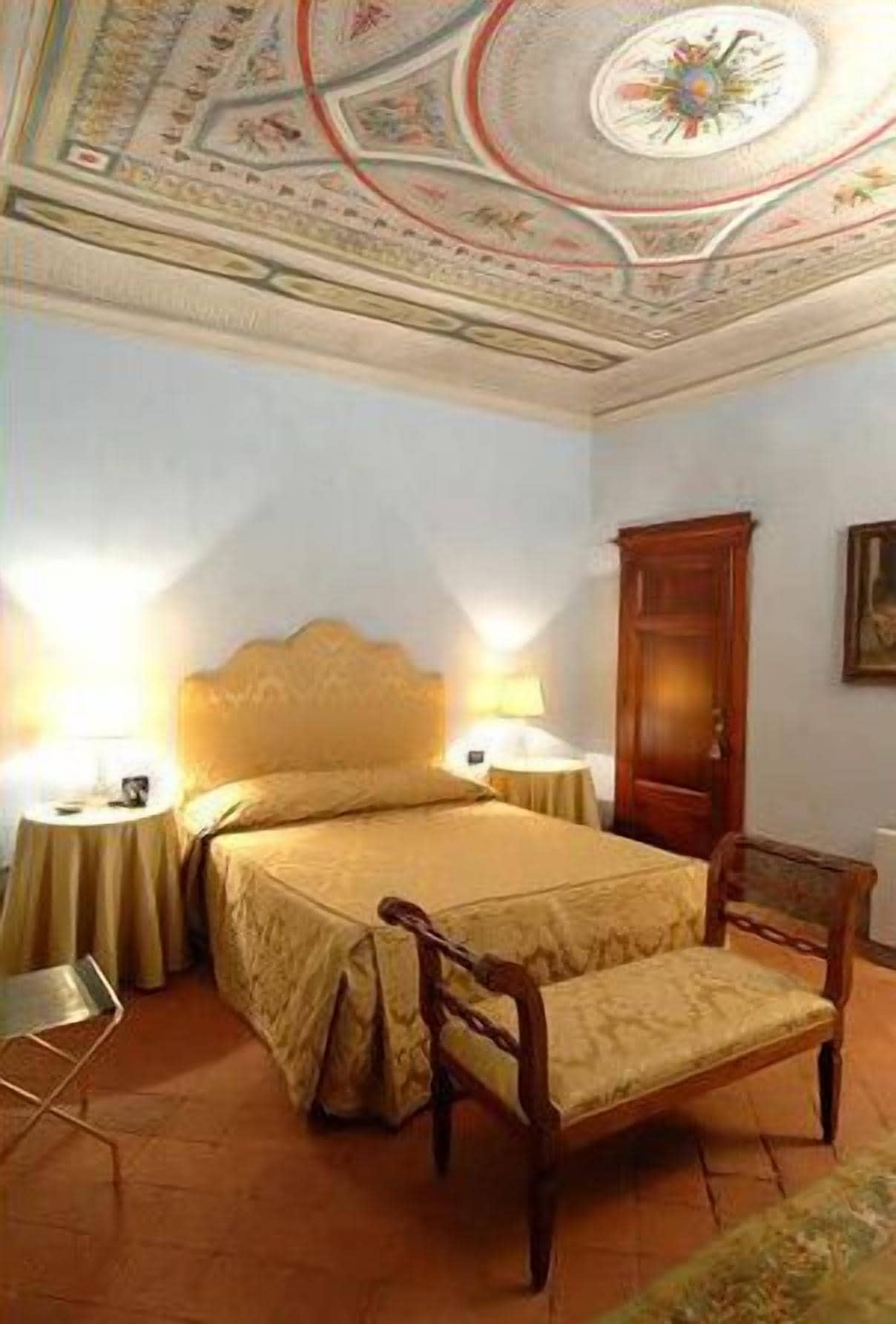 A bedroom with a large bed, two bedside lamps, a wooden chair, and a wooden wardrobe.