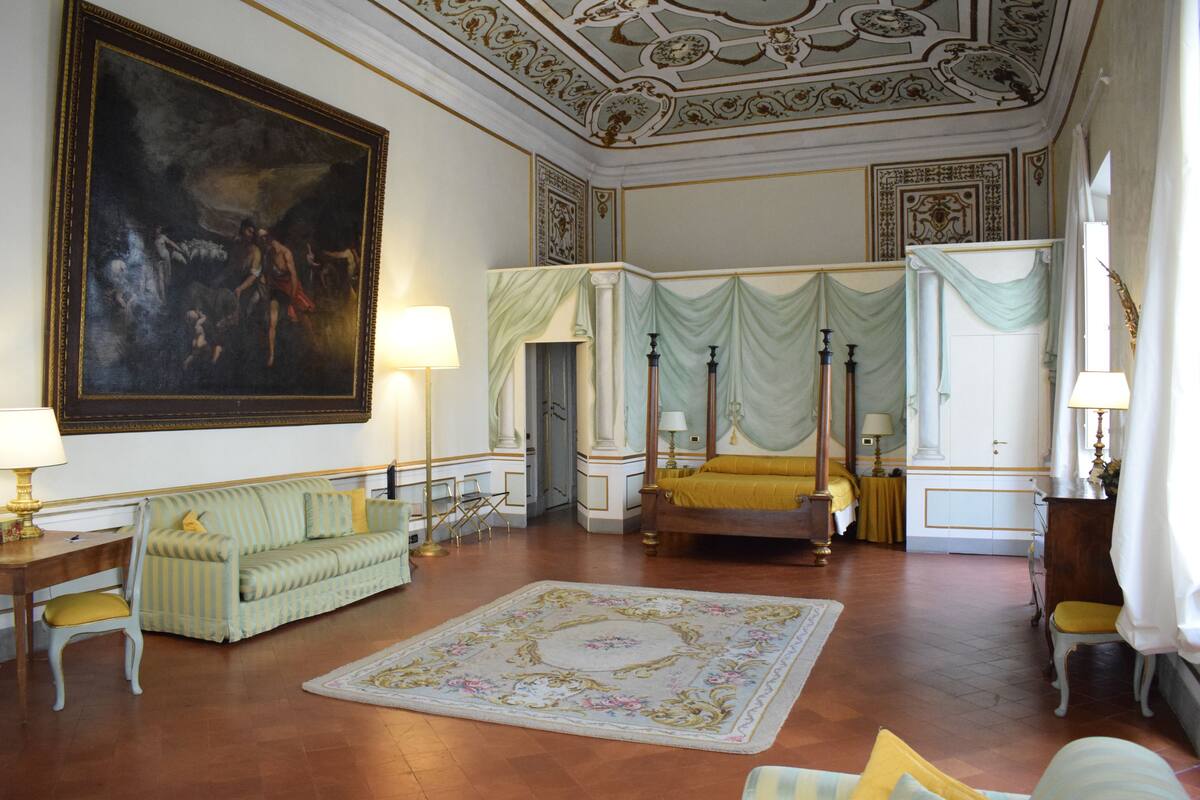 Una habitación amplia con un cuadro grande, una cama con dosel, un sofá y una alfombra decorativa.