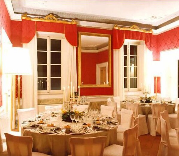 Une salle à manger élégante, avec des tables rondes dressées pour le repas, des murs rouges et un grand miroir.