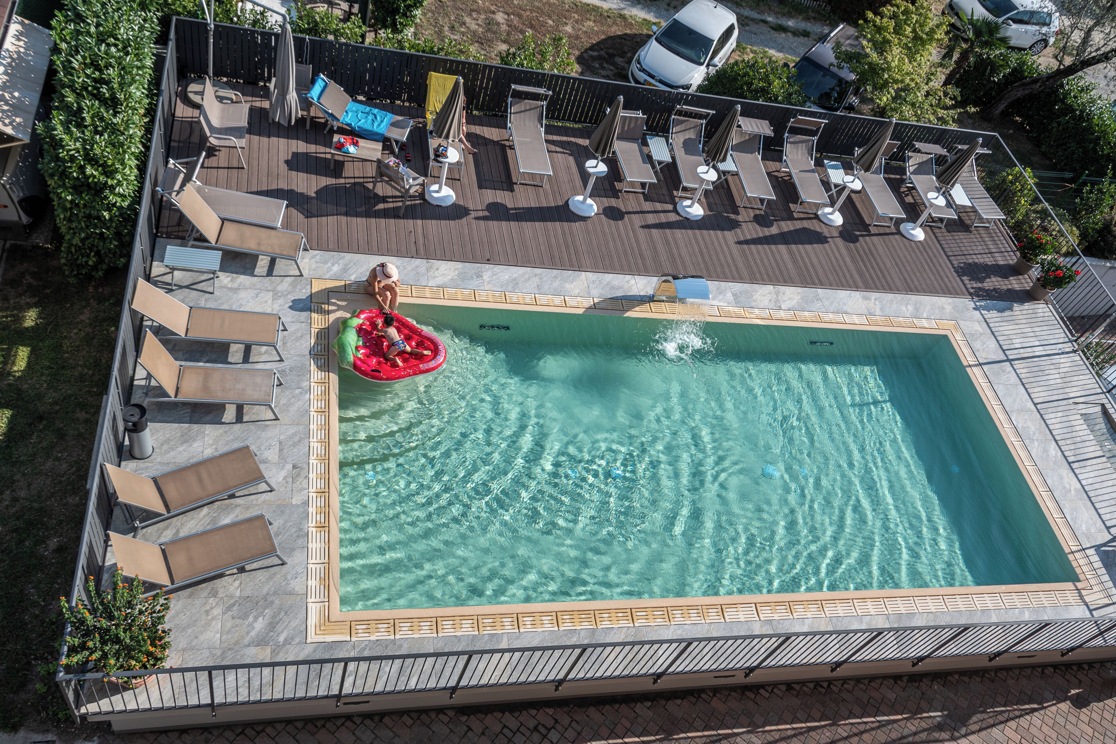 Vue aérienne d’une piscine avec des chaises longues et un radeau gonflable rouge.