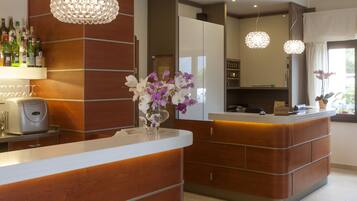 A modern reception area with a wooden reception desk, a bar area with bottles, and a decorative chandelier.