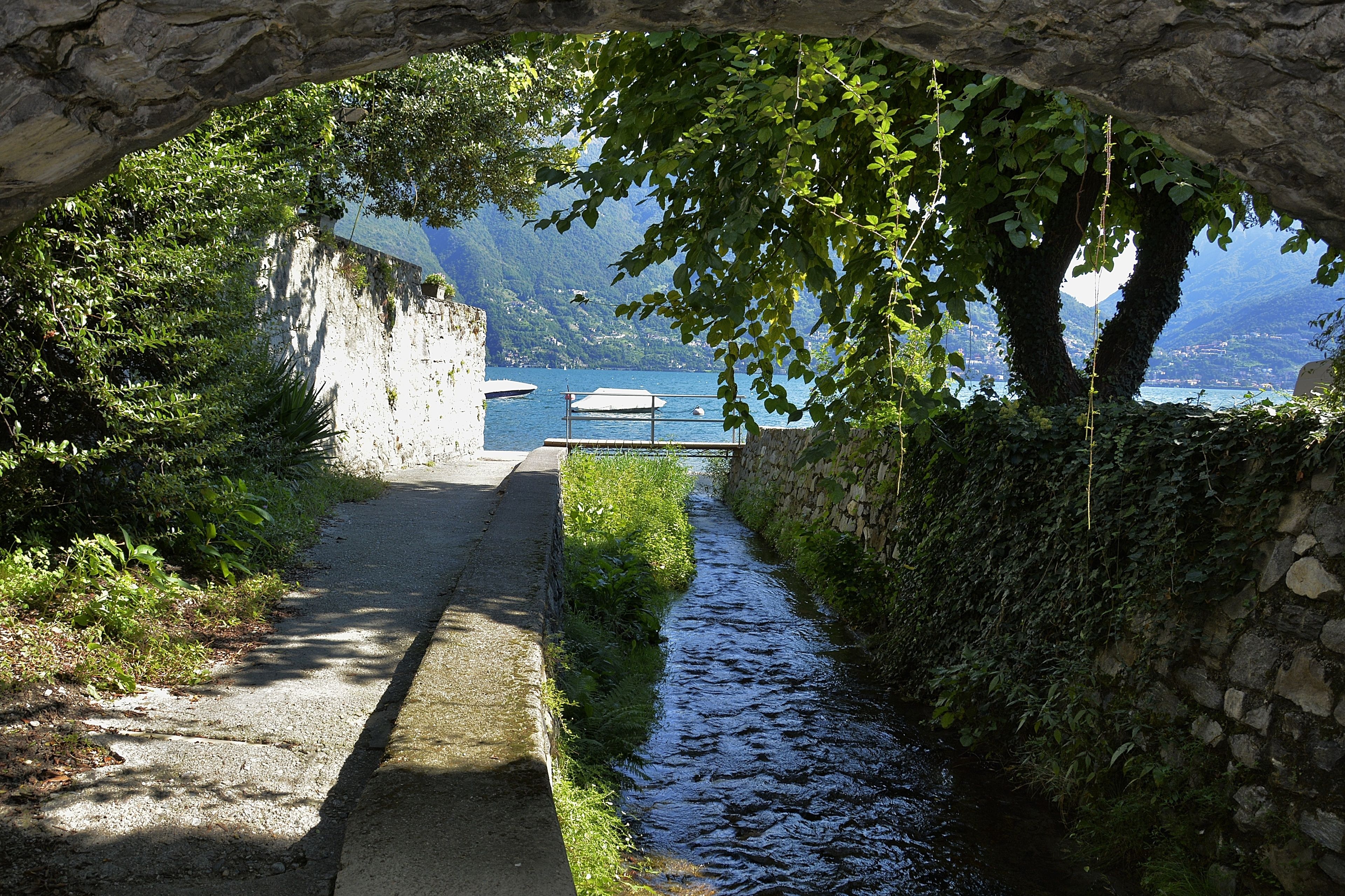 Un sentier de pierres menant à un plan d’eau, bordé de verdure et entouré d’un mur de pierres.