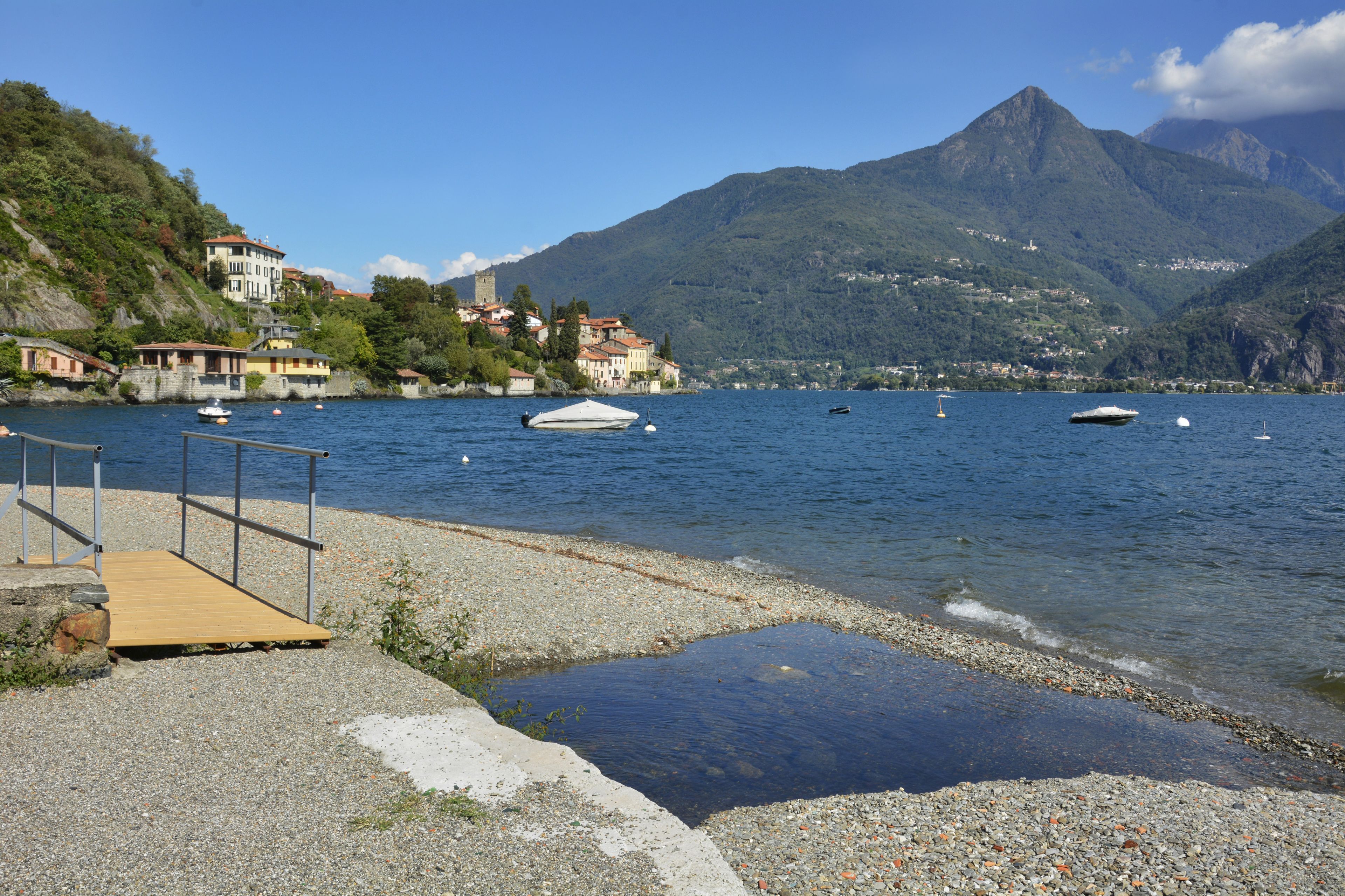 A lakeside view with boats, a wooden dock, and buildings on a hillside.