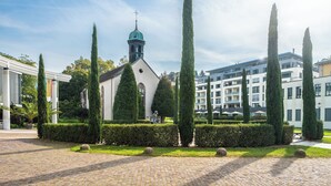 A church with a tall bell tower, surrounded by neatly trimmed hedges and tall cypress trees. - Aqua Aurelia Suitenhotel an den Thermen (Baden-Baden)