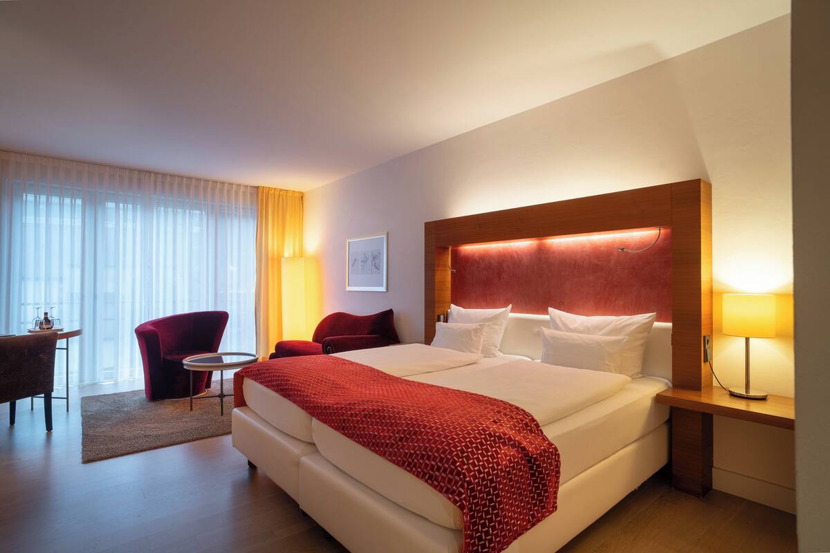 A hotel room with a large bed, a desk, a chair, and a window with curtains.