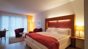 Una habitación de hotel con una cama grande, un escritorio, una silla y un ventanal con cortinas.
