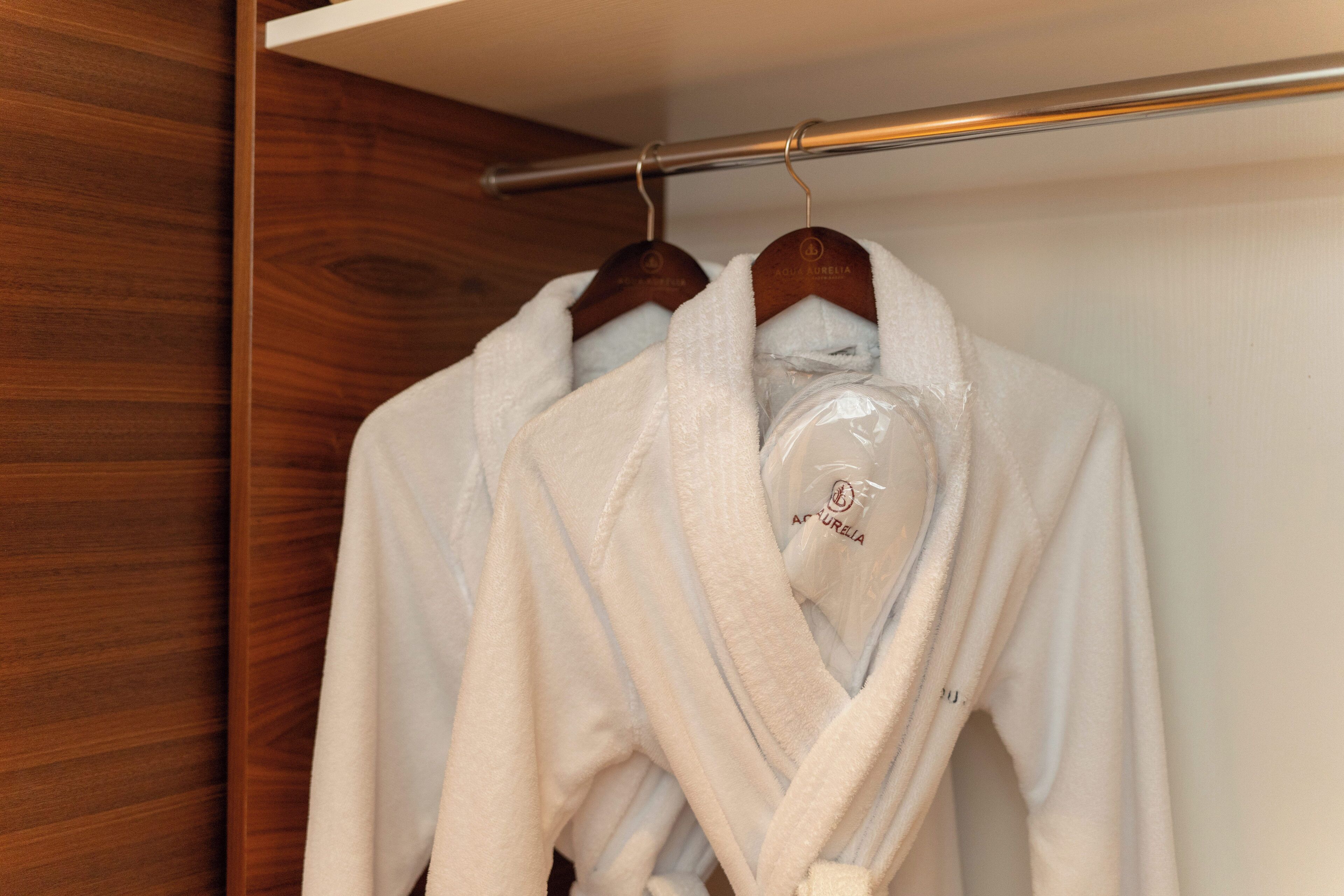 Een houten garderobe met twee witte gewaden aan een metalen stang.