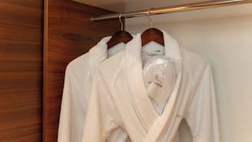 Een houten garderobe met twee witte gewaden aan een metalen stang.