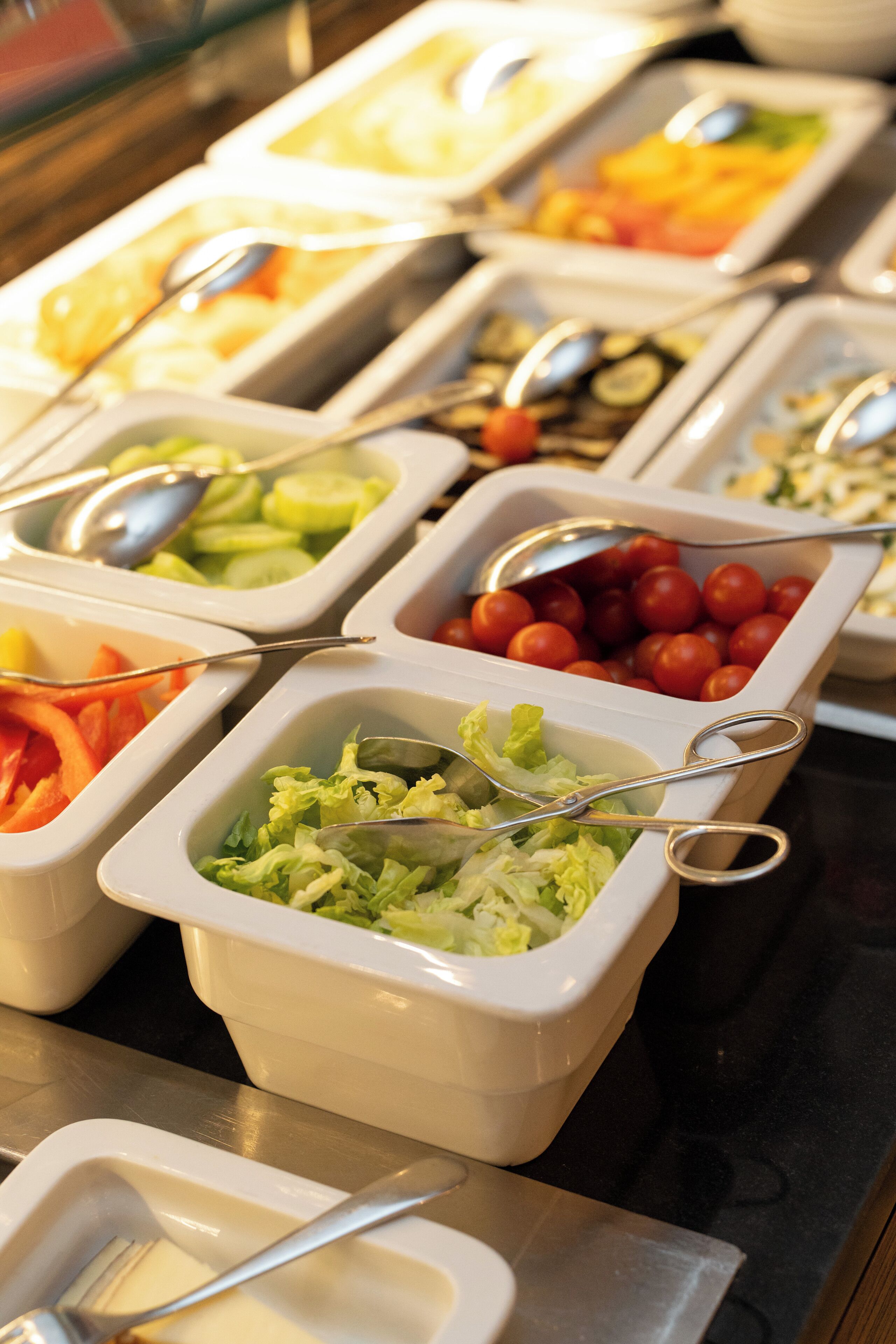 Een buffet met diverse soorten eten in witte bakken, elk met een lepel.