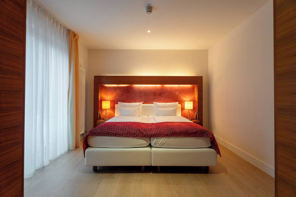 A double bed with a wooden headboard, two bedside lamps, and a red patterned throw blanket.