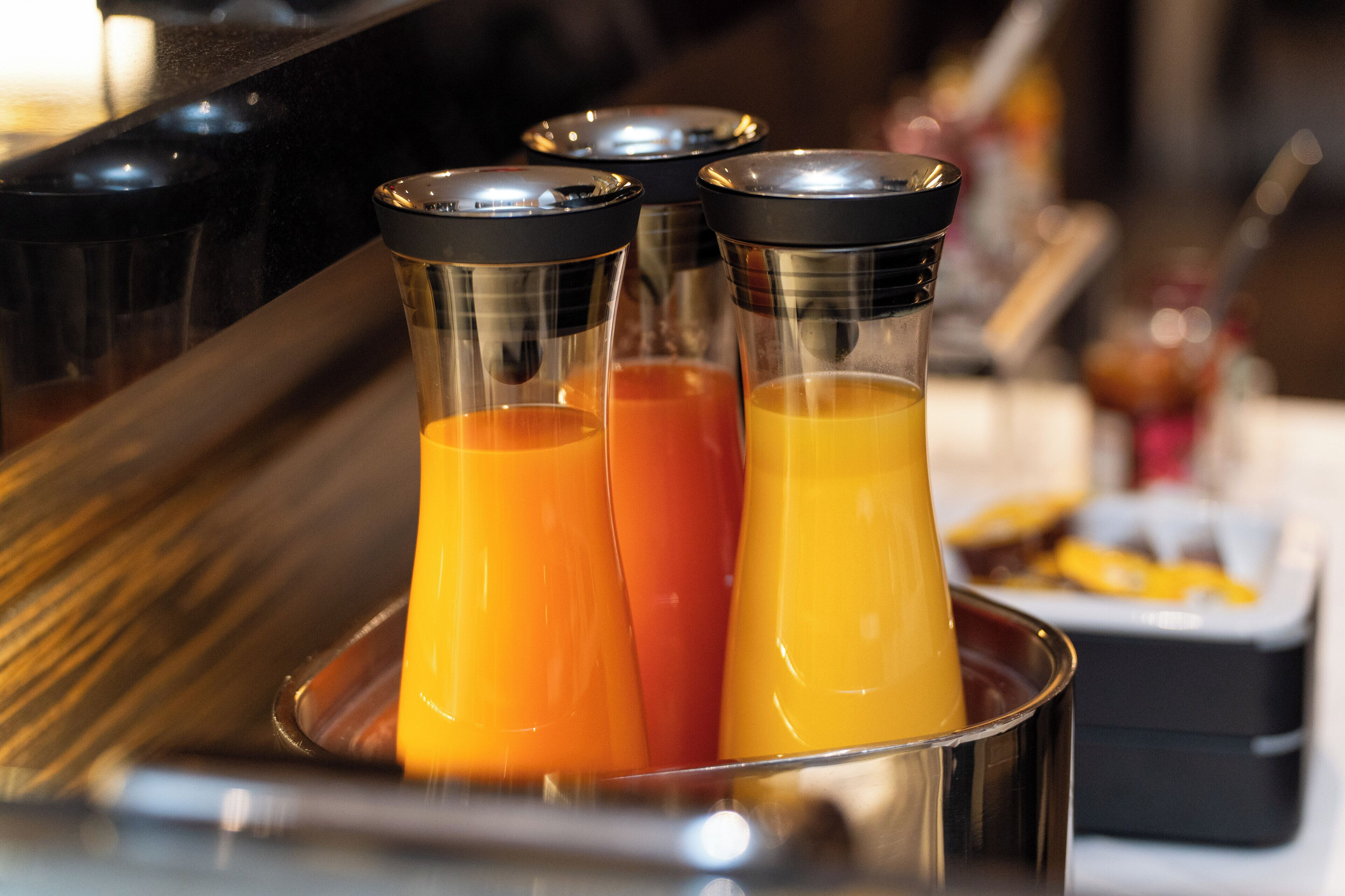 Three glass containers with orange liquid, likely juices, in a metal holder.