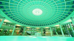 A spacious indoor area with a large glass dome ceiling, a central fountain, and multiple levels with balconies. - Aqua Aurelia Suitenhotel an den Thermen (Baden-Baden)