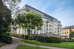 A multi-story residential building with balconies, a paved pathway, and well-maintained greenery.