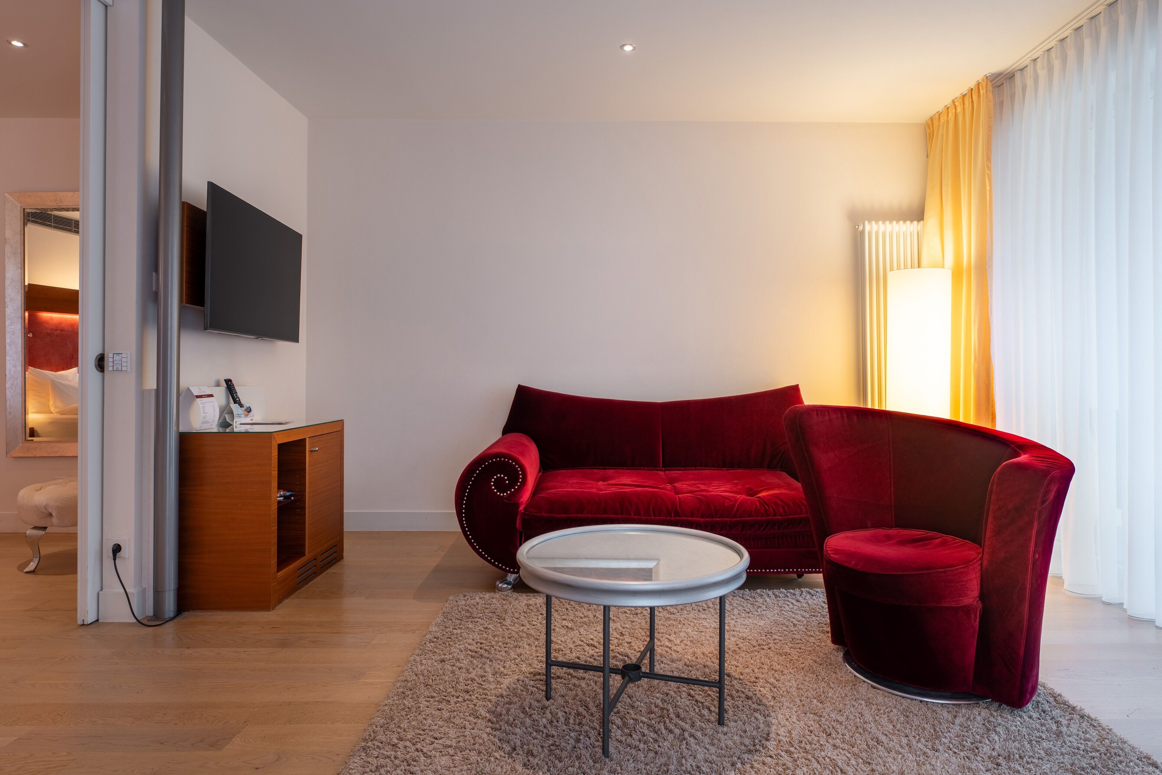 A modern living room with a red sofa, a small round table, and a TV mounted on the wall.