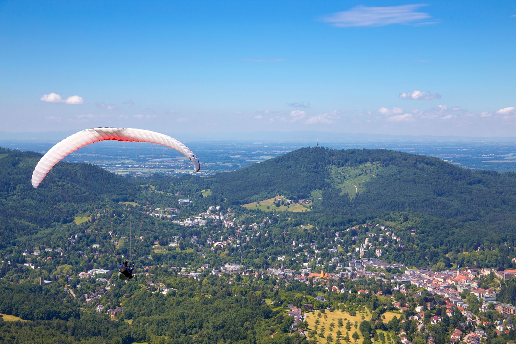 A person paragliding over a town surrounded by hills.