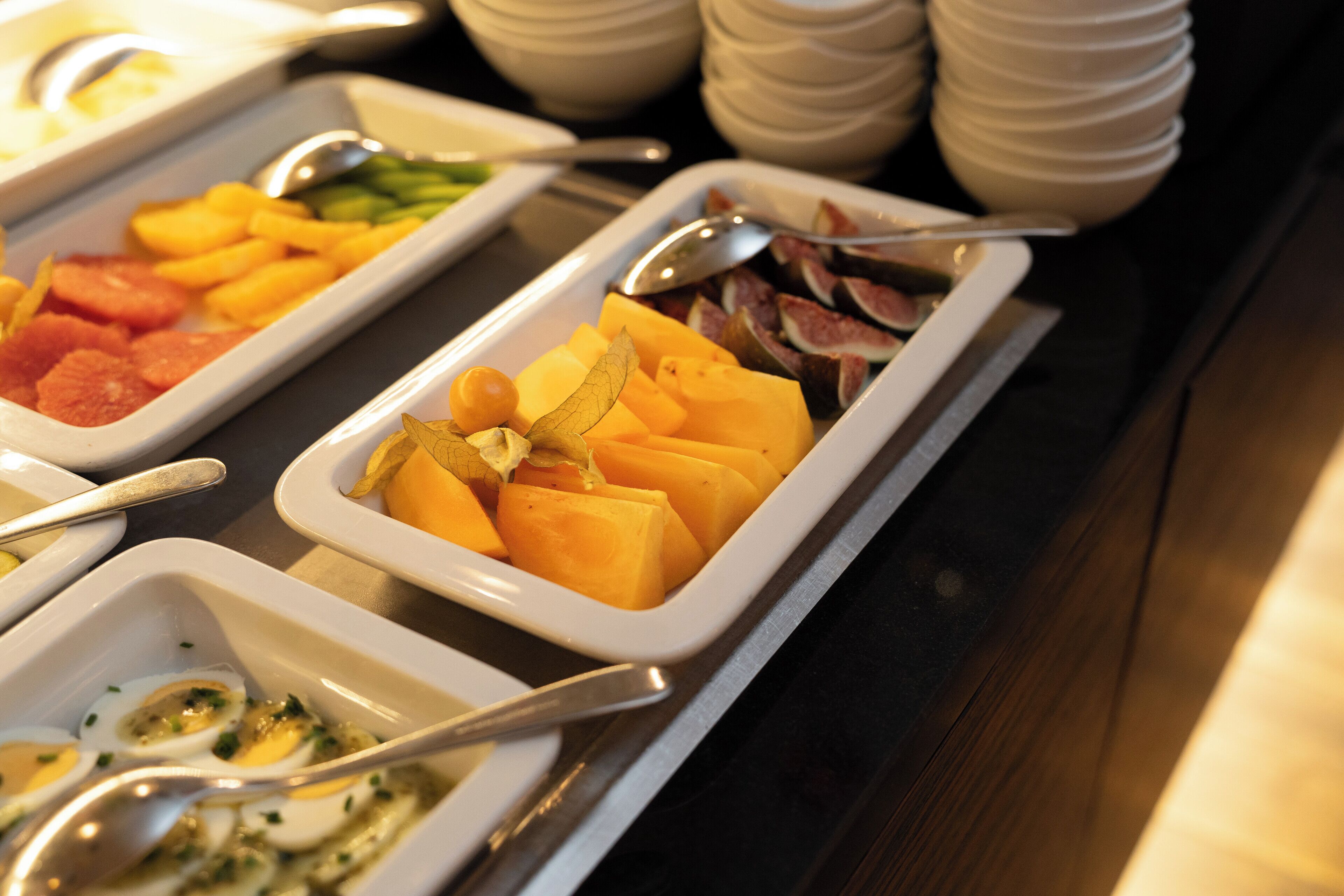 Un bufé con distintos alimentos, incluyendo frutas, verduras y huevos.