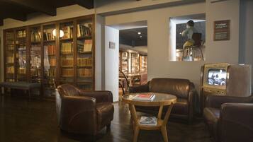 Een bibliotheek met leren fauteuils, een ronde houten tafel en boekenkasten vol boeken.