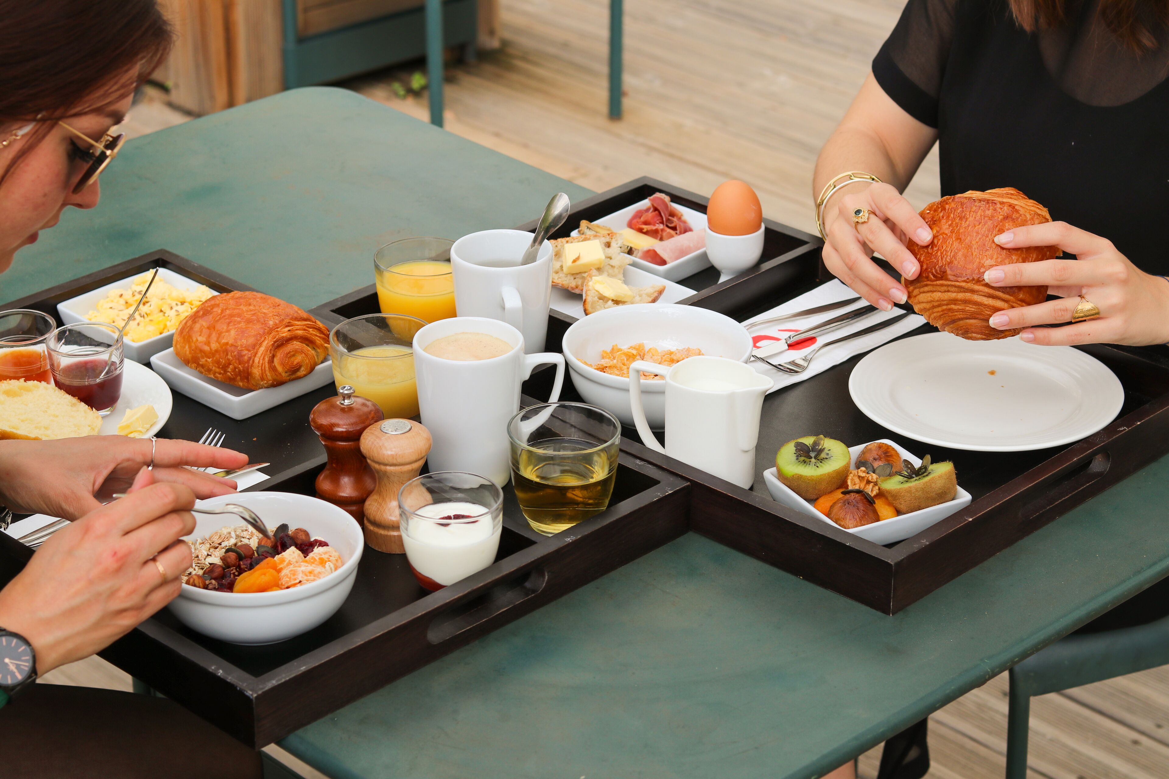 A breakfast tray with croissants, eggs, and fruit on a wooden table.