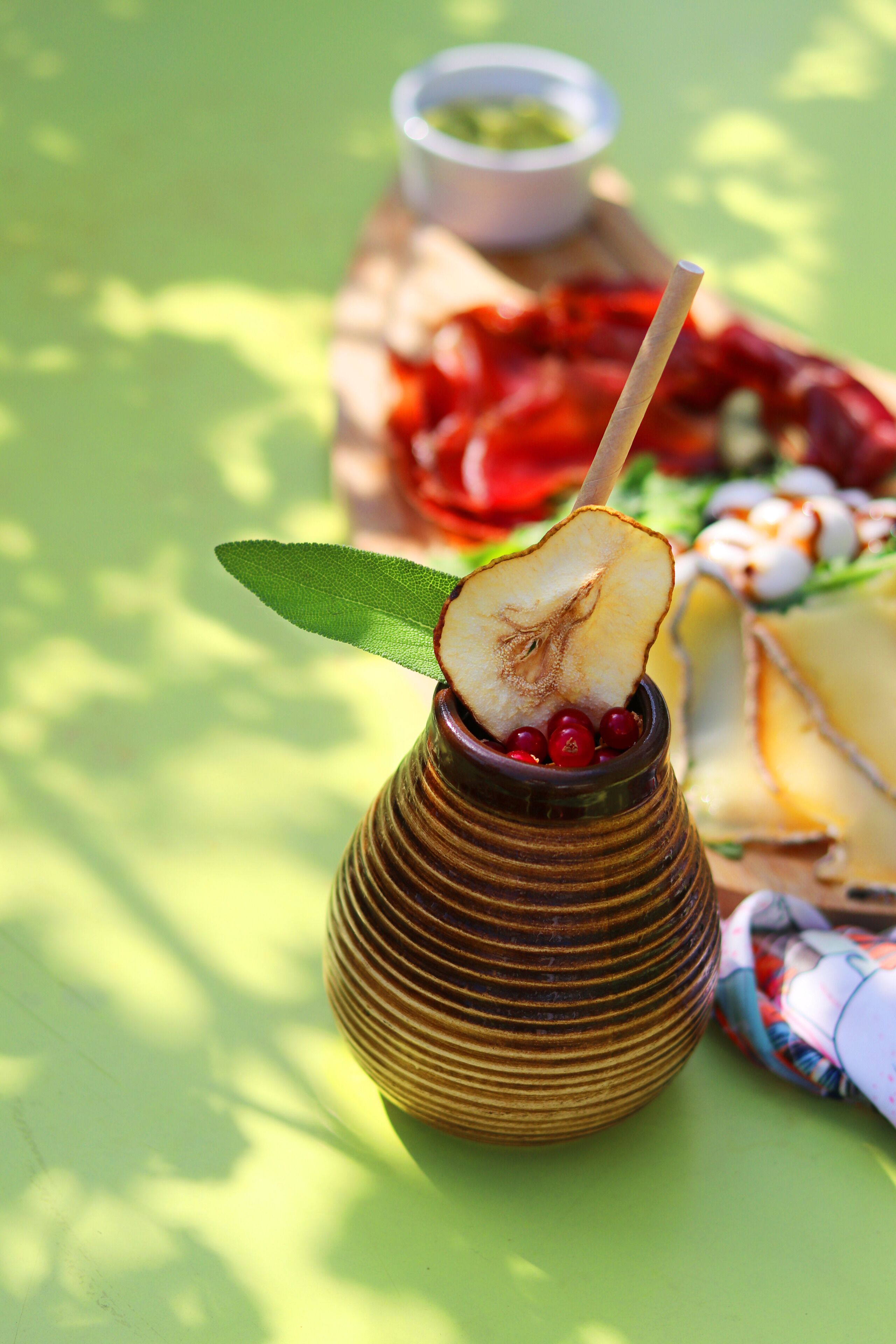 A traditional drink in a ceramic cup with a straw, garnished with a leaf and berries, on a green surface with a blurred background.