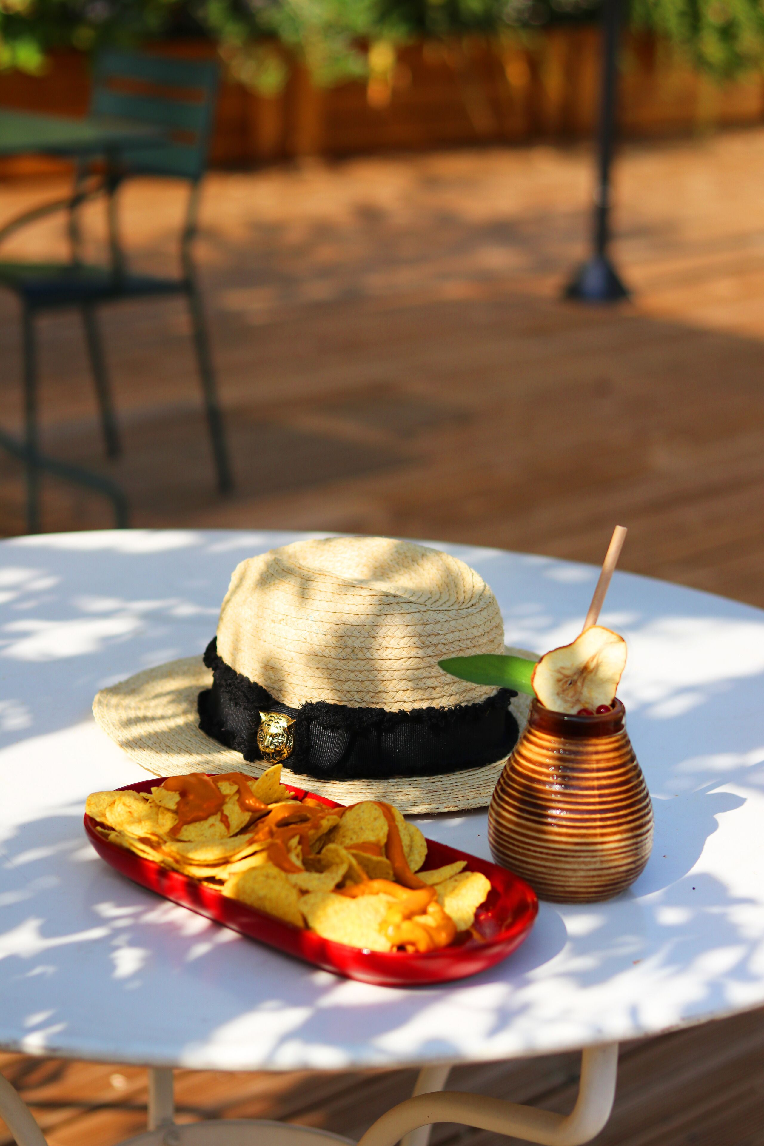 Una mesa con un sombrero de paja, un cuenco rojo de patatas fritas y un gotero de miel con fruta.