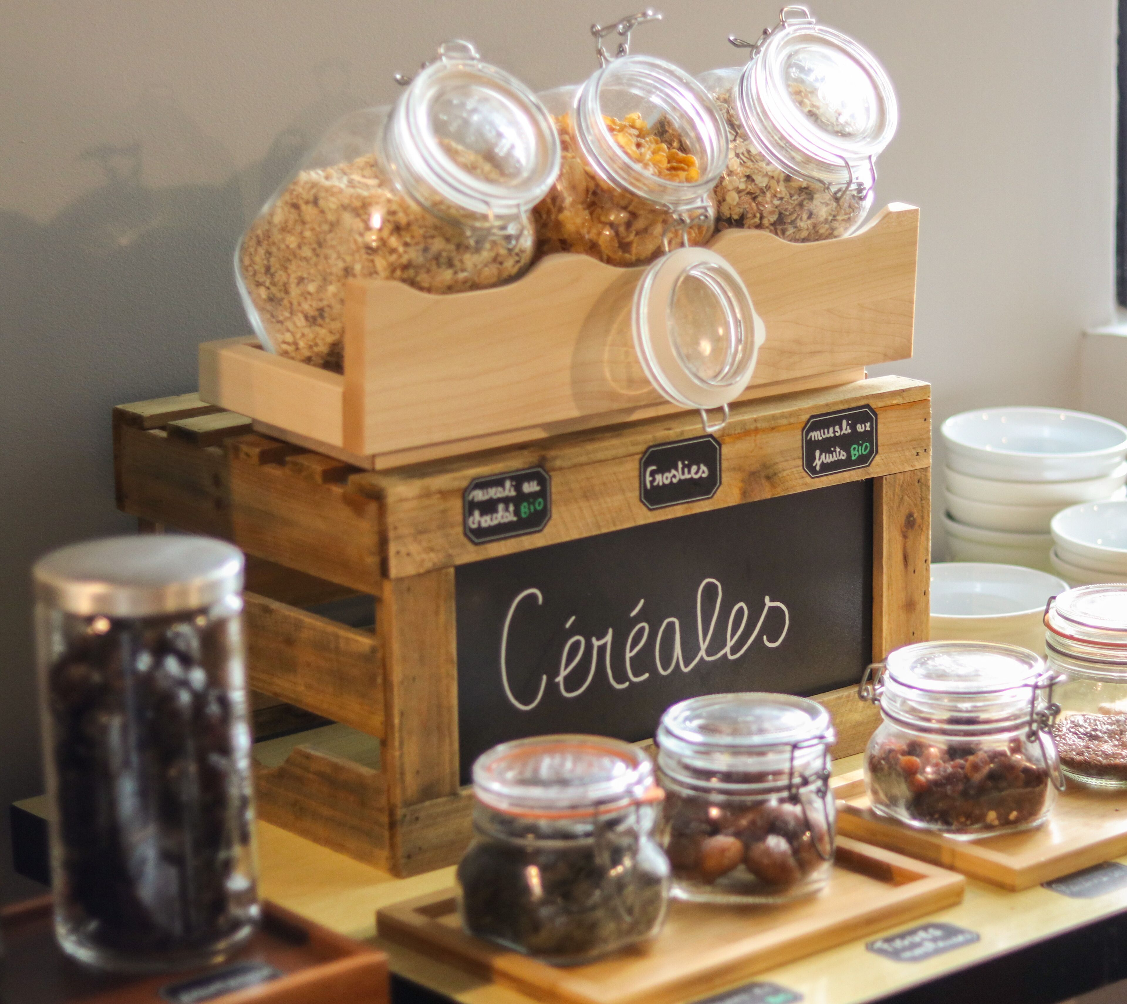 Esposizione di diversi prodotti alimentari, tra cui vasetti di noci e frutta secca, con etichette come 'Frosties' e 'Céréales'.