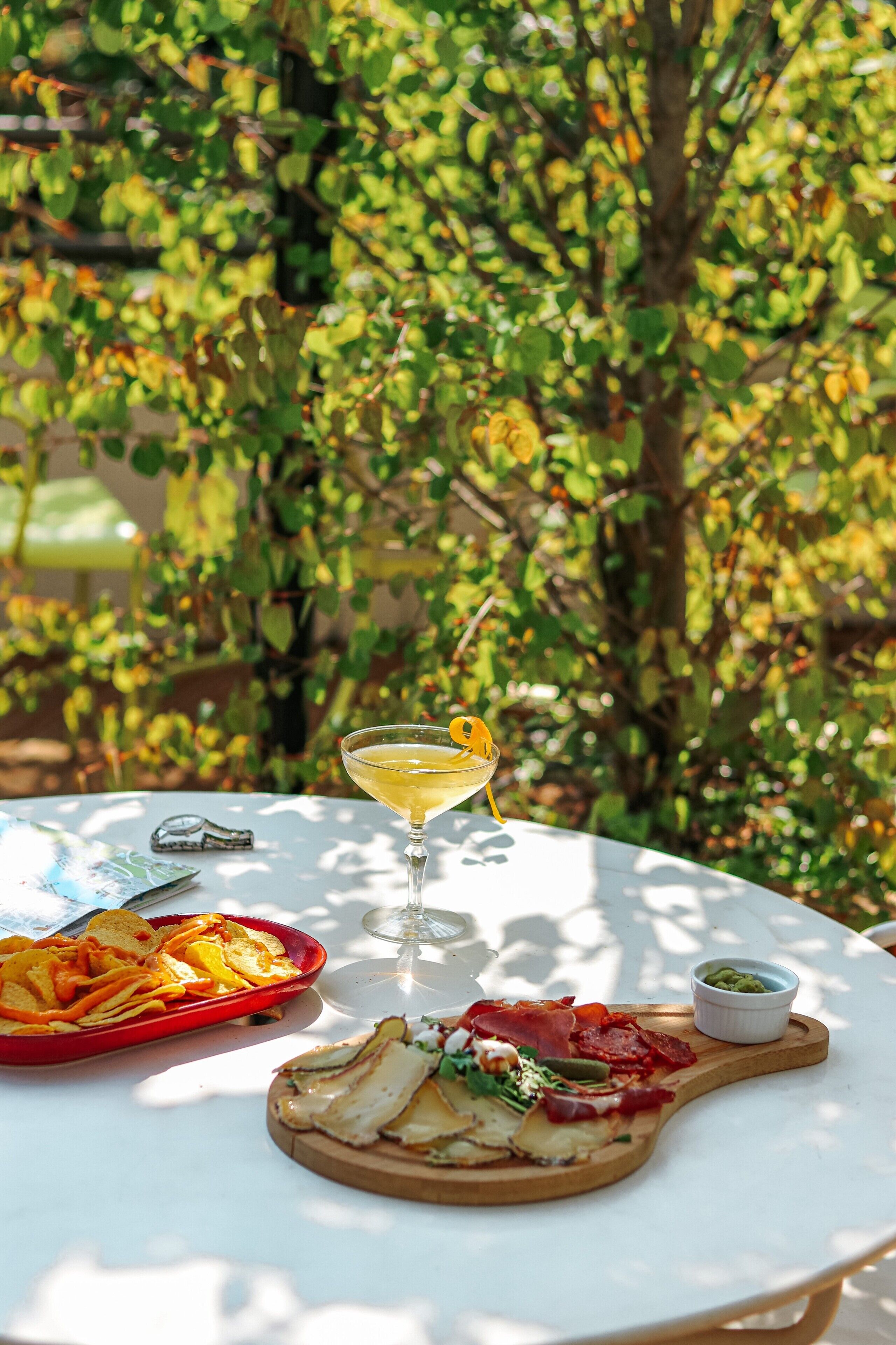 Una mesa con una copa de martini, una tabla de madera con comida y un plato rojo con papas fritas.