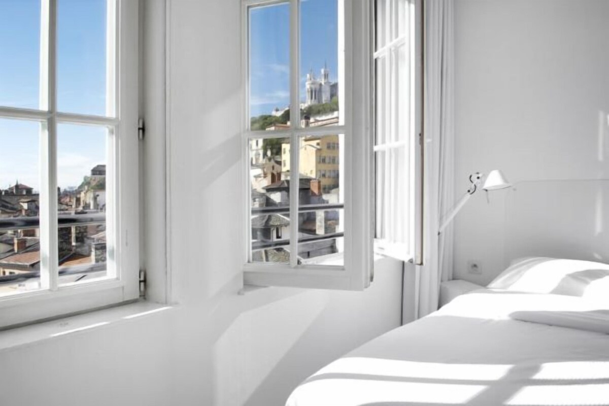 A bedroom with a large window, a bed, and a bedside lamp.