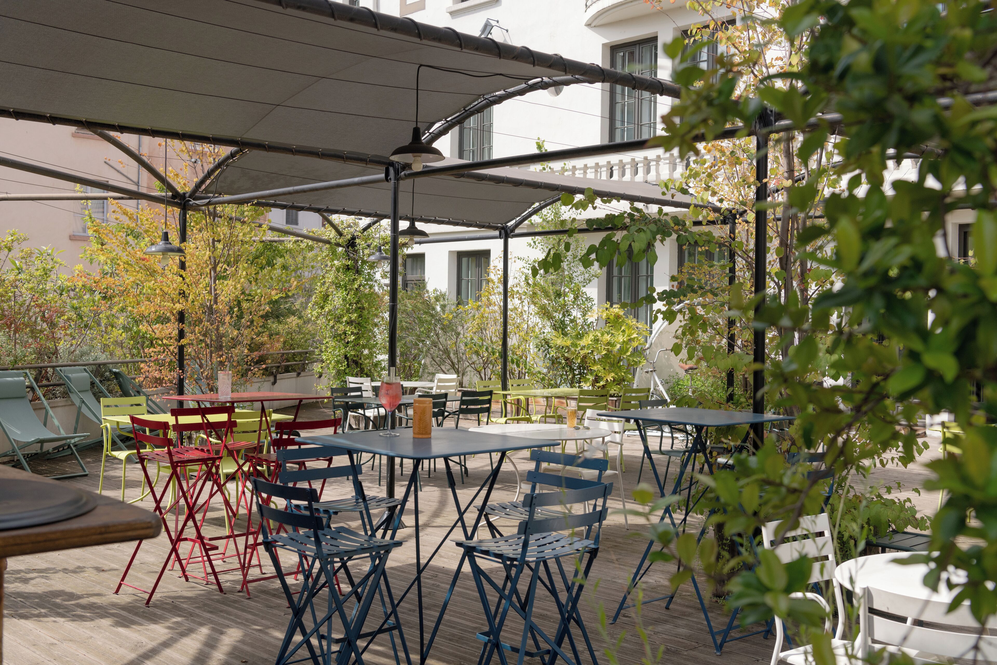 Un espace extérieur aménagé en terrasse, avec des tables et des chaises, un coin salon abrité et une vue sur les bâtiments en arrière-plan.