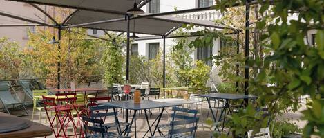 An outdoor patio area with tables and chairs, a covered seating area, and a view of buildings in the background.