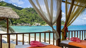 Habitación de hotel frente a la playa con vistas a aguas turquesas y una estructura de techo de paja.
