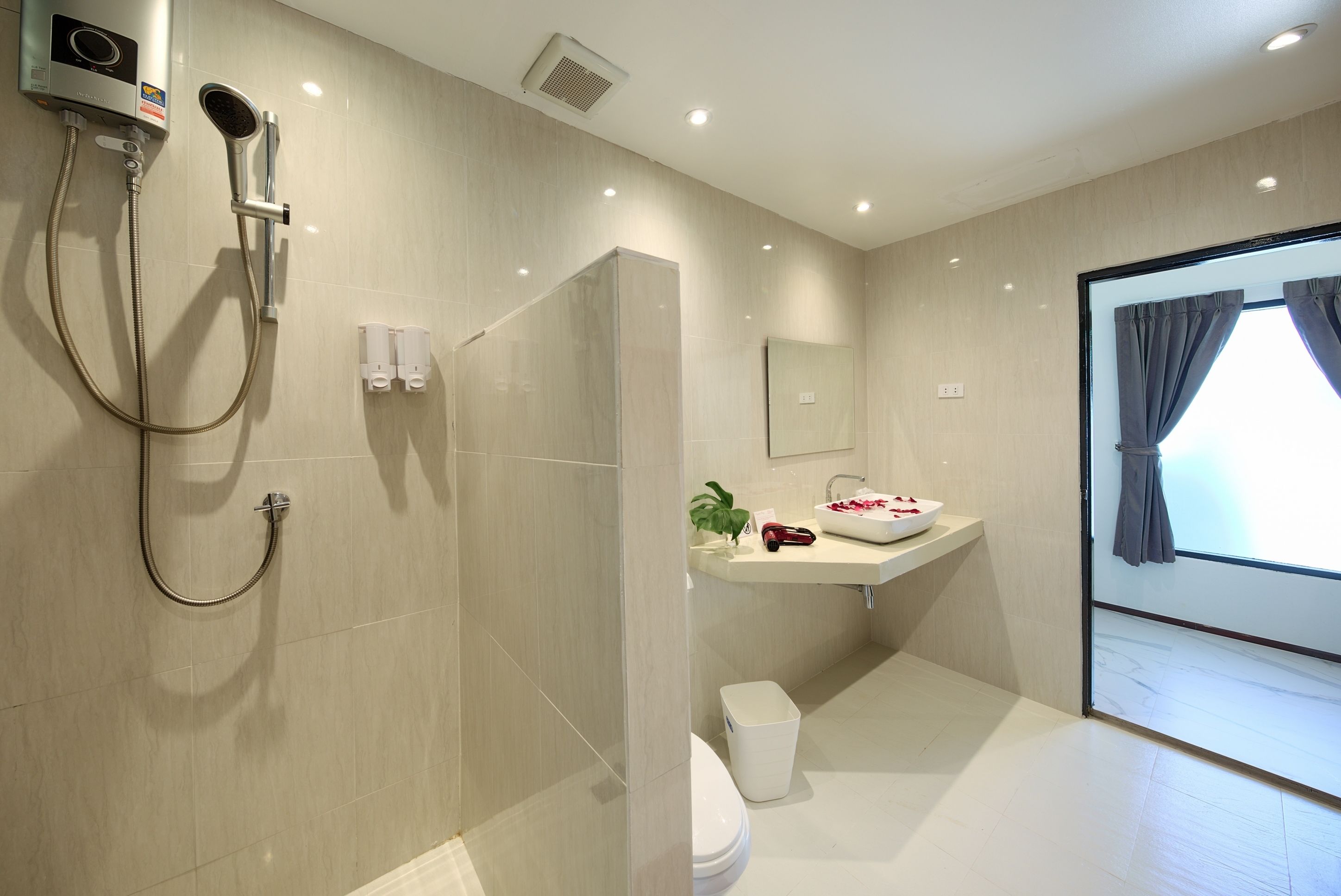A modern bathroom with a shower, toilet, sink, and a large window with curtains.